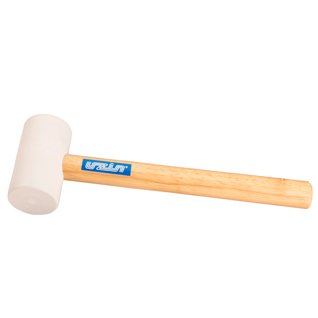 UZIN_Dummy_rubber hammer-UZIN_2014-11 Photo produit en gros plan d'un maillet en caoutchouc : tête beige clair en caoutchouc montée sur un manche en bois clair et lisse avec un autocollant de marque bleu ; posé en diagonale sur fond blanc, l'éclairage doux révèle la texture du caoutchouc et le veinage du bois ; utilisé pour des frappes douces en menuiserie, montage ou pose de carrelage.