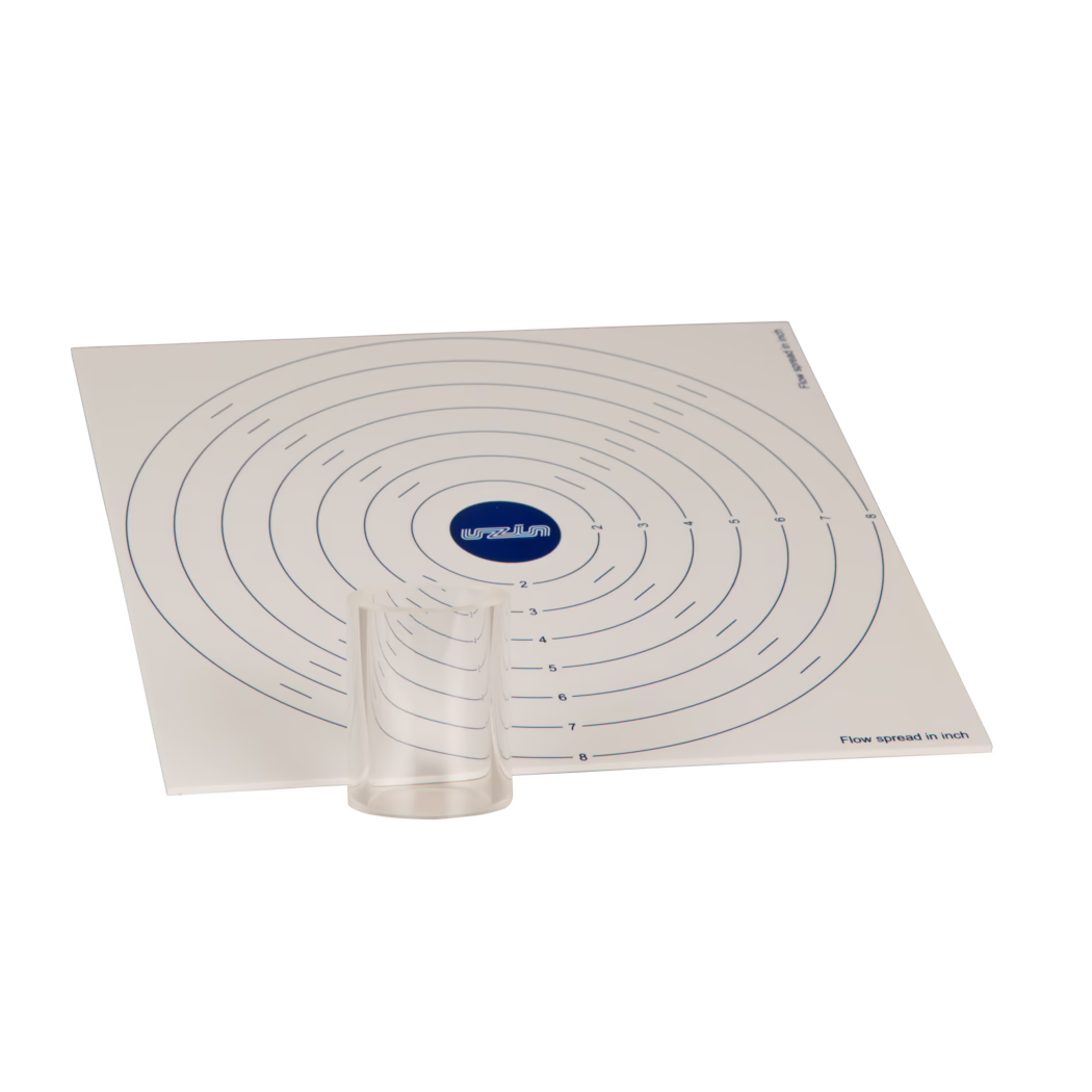 Un tapis de mesure carré blanc incliné avec des marques circulaires concentriques en bleu, un petit gobelet en plastique transparent placé près du bas au centre et un logo bleu au centre ; les anneaux sont numérotés et la mention 'Flow spread in inch' est visible en bas à droite.